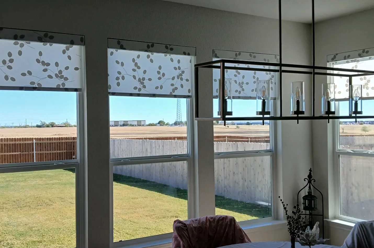 Top-down roller shades with a leaf-vine pattern in a sunlit dining area